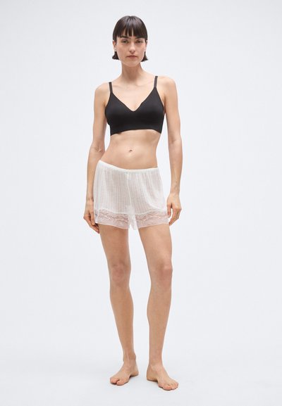 Črni bralette s tankimi naramnicami, kombiniran z belimi kratkimi hlačami z čipkastim robom. Mehka tkanina s subtilno teksturo, oprijet kroj in lahkoten videz.