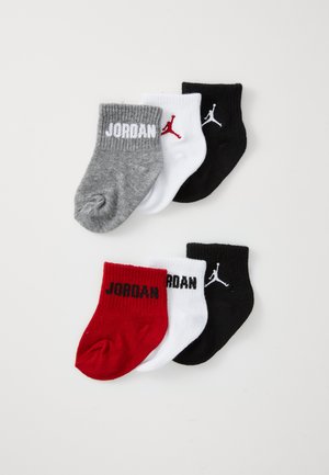 Ensemble de quatre chaussettes en coton pour bébé, de couleur gris, blanc, rouge et noir. Présente le texte "JORDAN" et des logos, hauteur cheville et bords ribbed.