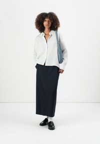 Chemise à rayures claires, jupe longue navy, mocassins noirs et sac à bandoulière bleu. Textures lisses, coupe décontractée et design casual.