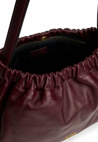 Bordeaux læderhåndtaske med en samlet design, viser en lynlåslomme indeni og glat tekstur. Guld hardware accent synlig.