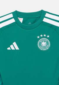Zelený fotbalový dres s bílým logem Adidas na levé straně hrudi a emblémem Německé fotbalové asociace se čtyřmi hvězdami na pravé straně hrudi.