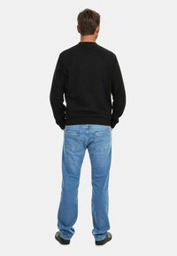 Black sweatshirt, long sleeves, round neckline; light blue jeans, straight leg, denim wash; black shoes with textured soles.