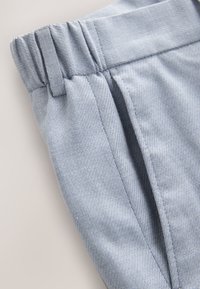Hellblaue, strukturierte Stoffhose mit einem elastischen Bund und seitlichen Falten. Nahaufnahme, die Material- und Nähdetails hervorhebt.
