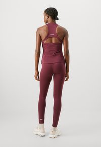 Bordeaux sportstopp med racerback-design och utskärning, ihopparad med matchande leggings. Lätt, stretchigt tyg med logotypdetaljer.