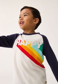 Bela majica z mornarsko modrimi rokavi, na kateri je napis »HAPPY« v belem, pod njim pa barvne diagonalne črte (rdeča, oranžna, rumena, turkizna).