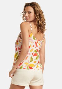 Blumen-Camisole mit mehrfarbigen Blattmustern in Pink, Rot, Gelb und Grün, mit dünnen Trägern und entspannter Passform, kombiniert mit strukturierten cremefarbenen Shorts.