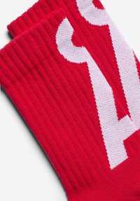 Rote gestrickte Socken mit Rippenstruktur, mit einem großen weißen Logo-Design. Der Stoff ist glatt, hat saubere Kanten und leuchtende Farbe.