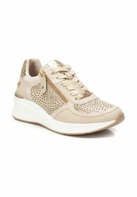 Zapatilla beige con un diseño perforado, acentos metálicos, cierre de cordones y cremallera lateral. Suela gruesa blanca con una suela de goma texturizada.