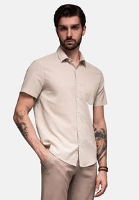 Korte mouwen, lichtbeige knoopshirt van zachte stof, met een borstzak en een gladde textuur, gecombineerd met lichtgekleurde broek.