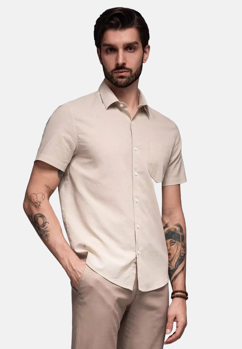 Korte mouwen, lichtbeige knoopshirt van zachte stof, met een borstzak en een gladde textuur, gecombineerd met lichtgekleurde broek.