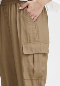 Beiga cargobyxor med en vida ben-design, som har en elastisk midja och en stor ficka på sidan. Slät, hållbar tyg.