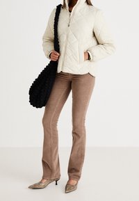 Vatteret cremefarvet jakke, lysebrune fløjlsleggings med vidde, metalliske spidse hæle og en struktureret sort skuldertaske.