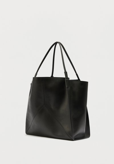 Sac fourre-tout en cuir noir avec doubles poignées fines et couture géométrique minimaliste, présenté sur un fond clair uni.