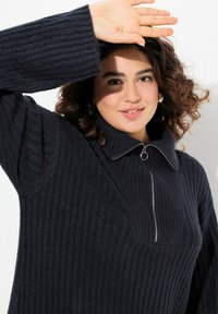 Pull en maille côtelée marine à manches longues, col zippé quart et tissu tricoté texturé. Doté d'une fermeture éclair avec un tirette accent circulaire.