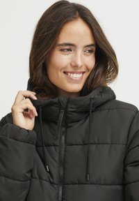 Giubbotto puffo nero con collo alto, chiusura con zip e cordini regolabili. Presenta un design trapuntato e una texture morbida.