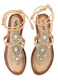 Sandali in pelle marrone con decorazioni in perline e gemme, design open-toe e lacci alla caviglia. Presentano una suola marrone texturizzata e accenti decorativi.