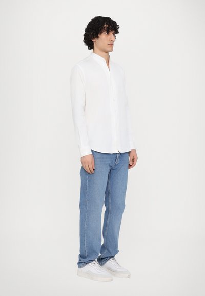Hvit langermet skjorte med knappestolpe og bandkrage, parret med lyseblå rette jeans og hvite sneakers. Enkelt, rent design.