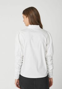 Maglione bianco con maniche a sbuffo e colletto arricciato. Materiale in cotone liscio con texture arricciata sulle maniche, design minimalista.