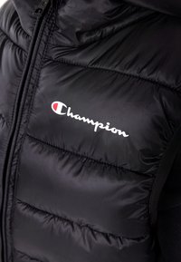 Czarna, puchowa kamizelka wykonana z gładkiego nylonu. Posiada pełny zamek błyskawiczny oraz biały logo "Champion" z czerwonym akcentem na piersi.