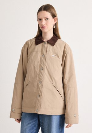 Giacca beige con colletto in velluto a coste marrone, bottoni a pressione, due tasche laterali e un sottile dettaglio del logo sul petto. Tessuto testurizzato.