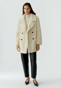 Cream-colored faux fur double-breasted coat with black buttons, two side pockets, paired with black leather pants and black heeled shoes.