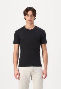 Sorte kortærmede T-shirt med rund halsudskæring, lavet af blødt stof. Båret med lyse jeans, der har et enkelt design og let tekstur.