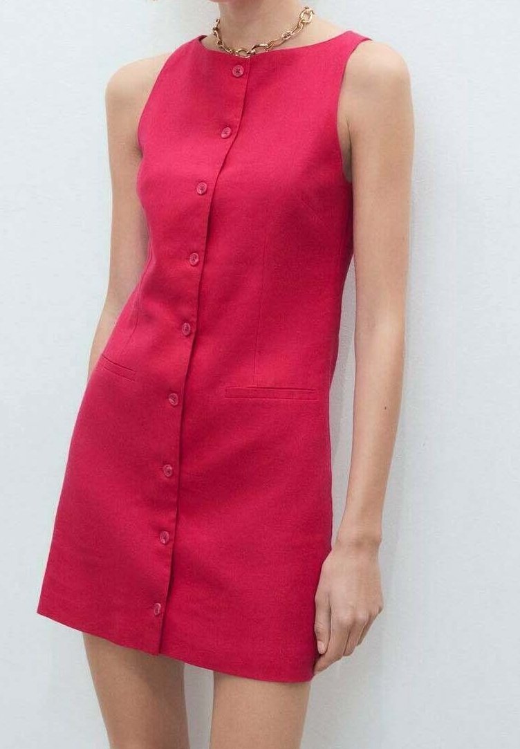 Robe sans manches rouge vif à boutons, avec poches devant, portée par une personne debout devant un fond blanc uni.