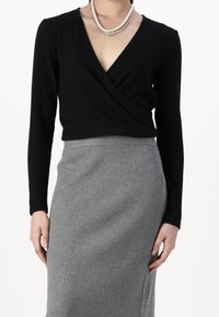 Svart långärmad omlottopp med v-ringning, kombinerad med en figurnära grå ribbad pennkjol. Mjuk textur, minimalistisk design.