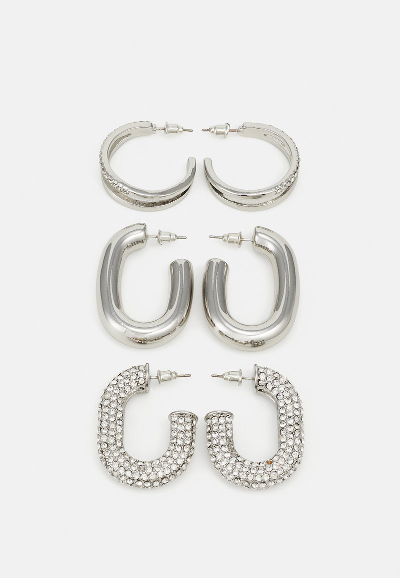 Quatre paires de boucles d'oreilles en argent : deux modèles de créoles lisses et brillantes, un modèle texturé et un autre recouvert de petits strass transparents.