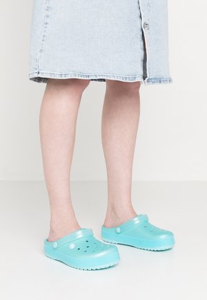 Sabots turquoise en matériau durable avec des trous de ventilation, design plat, et une large sangle croisée sur le dessus pour un maintien sécurisé.