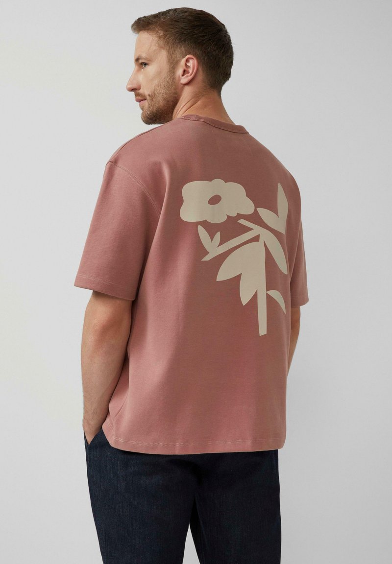 Rosa T-Shirt aus Baumwolle mit einem großen cremefarbenen Blumenmuster auf dem Rücken. Kurze Ärmel, lockere Passform, lässiger Stil.