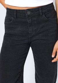 Svarta denimjeans med ett åtsittande midjeband, framtill fickor och knäppning med knapp. Tyget har en slät yta och en lätt blekt finish.