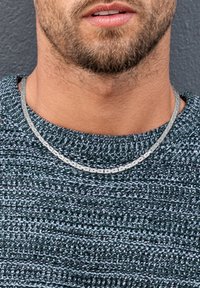 Silberne Kettenhalskette mit strukturierten Gliedern, getragen über einem dunkelgrünen Strickpullover. Nahaufnahme des Halsbereichs.