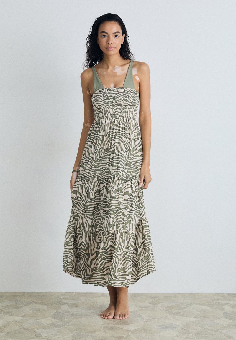 Maxi dress in light green and beige zebra pattern, featuring a smocked bodice and thick straps, with a flowy skirt and tiered hem.