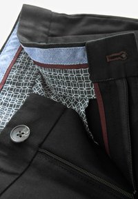Pantalon noir à texture lisse, avec une doublure détaillée à motif en gris et blanc, et un accent subtil bordeaux à la ceinture.