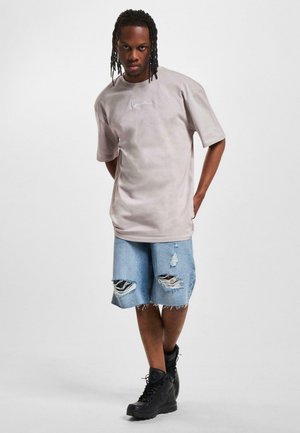 Light gray oversized t-shirt with embroidered accent, paired with distressed denim shorts. Black boots complete the look.