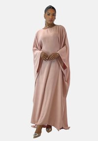 Long, flowing pink kaftan with wide sleeves, featuring a smooth, textured fabric. Paired with pointed heels adorned with embellishments.