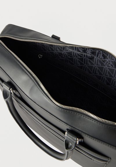 Mallette en cuir noir avec la fermeture éclair principale ouverte, révélant l'intérieur en tissu à motif et une poche zippée intérieure.