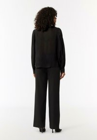 Black long-sleeve blouse with a smooth texture and buttoned cuffs, paired with black wide-leg trousers and stiletto heels, viewed from behind.