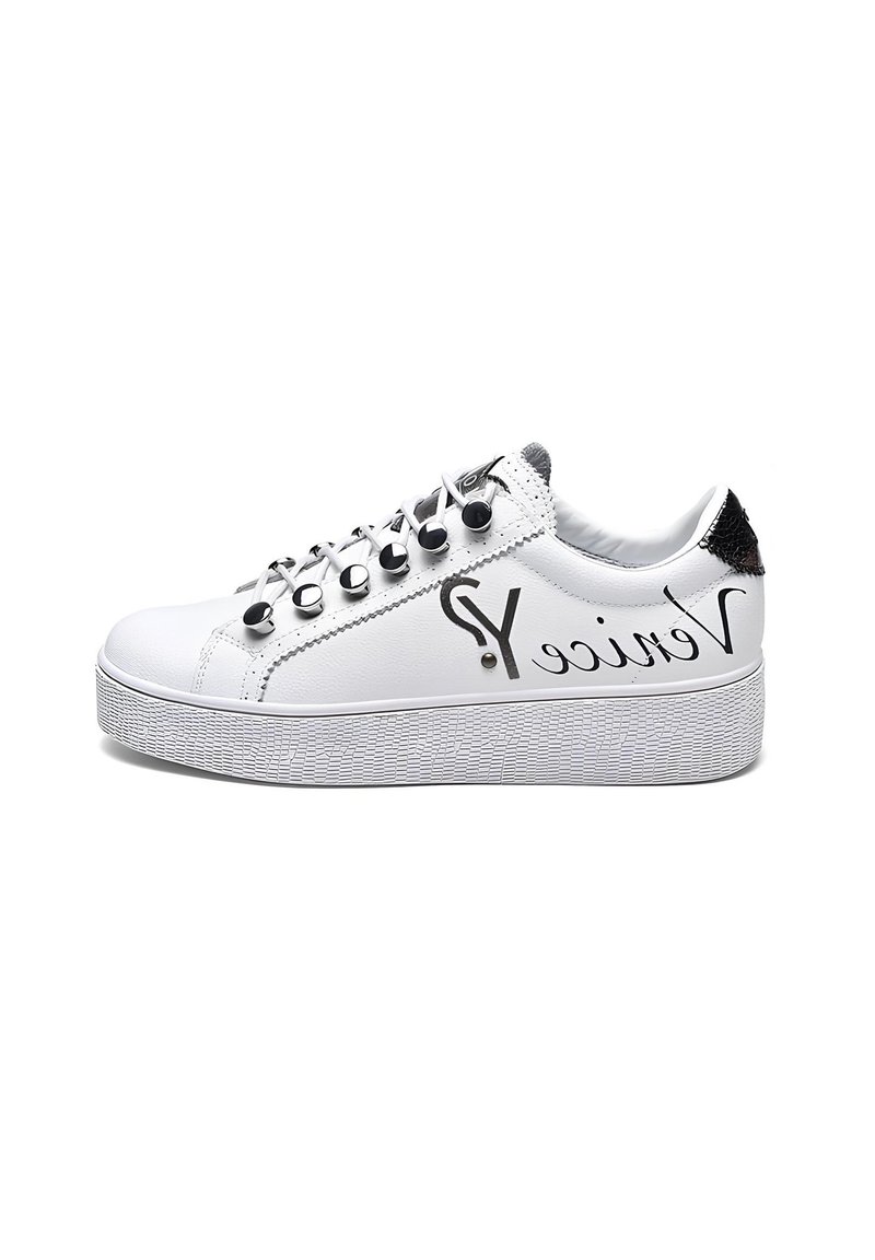 Sneaker bianca con suola piatta testurizzata, borchie metalliche sui lacci e dettagli neri sul tallone e sul lato. Presenta il logo sul lato esterno.