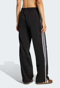 Czarne sportowe spodnie o luźnym kroju, z białymi paskami po bokach i elastycznym pasem. Materiał wygląda na gładki i lekki.