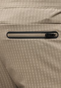 Gros plan d'une surface en tissu beige avec une poche zippée horizontale soulignée par un liseré noir.