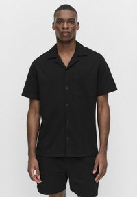 Korte-sleeve zwarte shirt met een notch-kraag, enkele borstzak en knoopsluiting, gemaakt van gestructureerde stof. Draag het met bijpassende shorts.