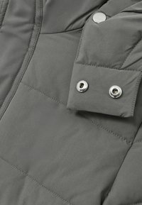 Pelēks pufīgs jakkas mētelis ar tuvplānu par piedurkni, kas rotāta ar snap pogām, gludu tekstūru un quilted dizaina detaļām.