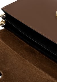 Borsa a mano in pelle marrone con una superficie liscia, hardware dorato e interno in suede nero. Presenta una forma strutturata e cuciture discrete.