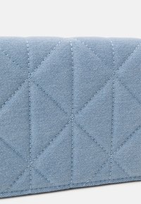 Tissu matelassé bleu clair avec des coutures diagonales et verticales formant des motifs en losange sur une surface douce et rembourrée.