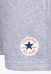 Γκρι βαμβακερό ύφασμα με στρογγυλό λογότυπο Converse All Star, ναυτική αστέρα, κόκκινες λεπτομέρειες και μαύρο κείμενο. Υφασμάτινα ρούχα καθημερινής χρήσης με υφή.