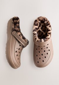 Brown plastic clogs featuring a leopard print faux fur lining, ventilation holes, and a side toggle strap for a secure fit.
