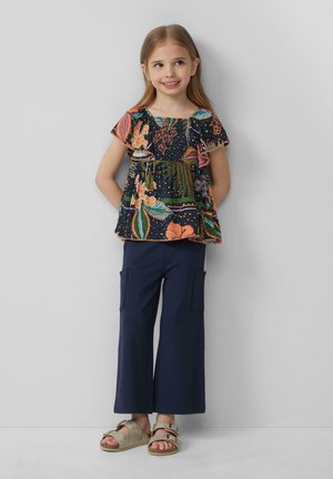 Haut foncé à motifs floraux avec des manches froncées, associé à un pantalon cargo large bleu marine. Des sandales beiges à doubles lanières complètent l'ensemble.