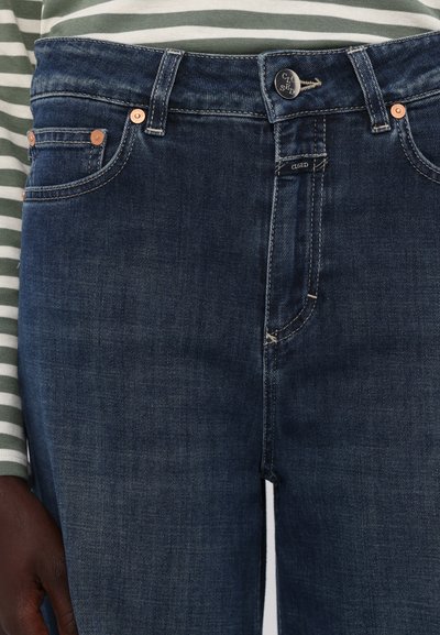 Mørk denim jeans med et klassisk fem-lomme design, som har kobbernitter og søm. Livet har en metallknapp og logo-detalj.